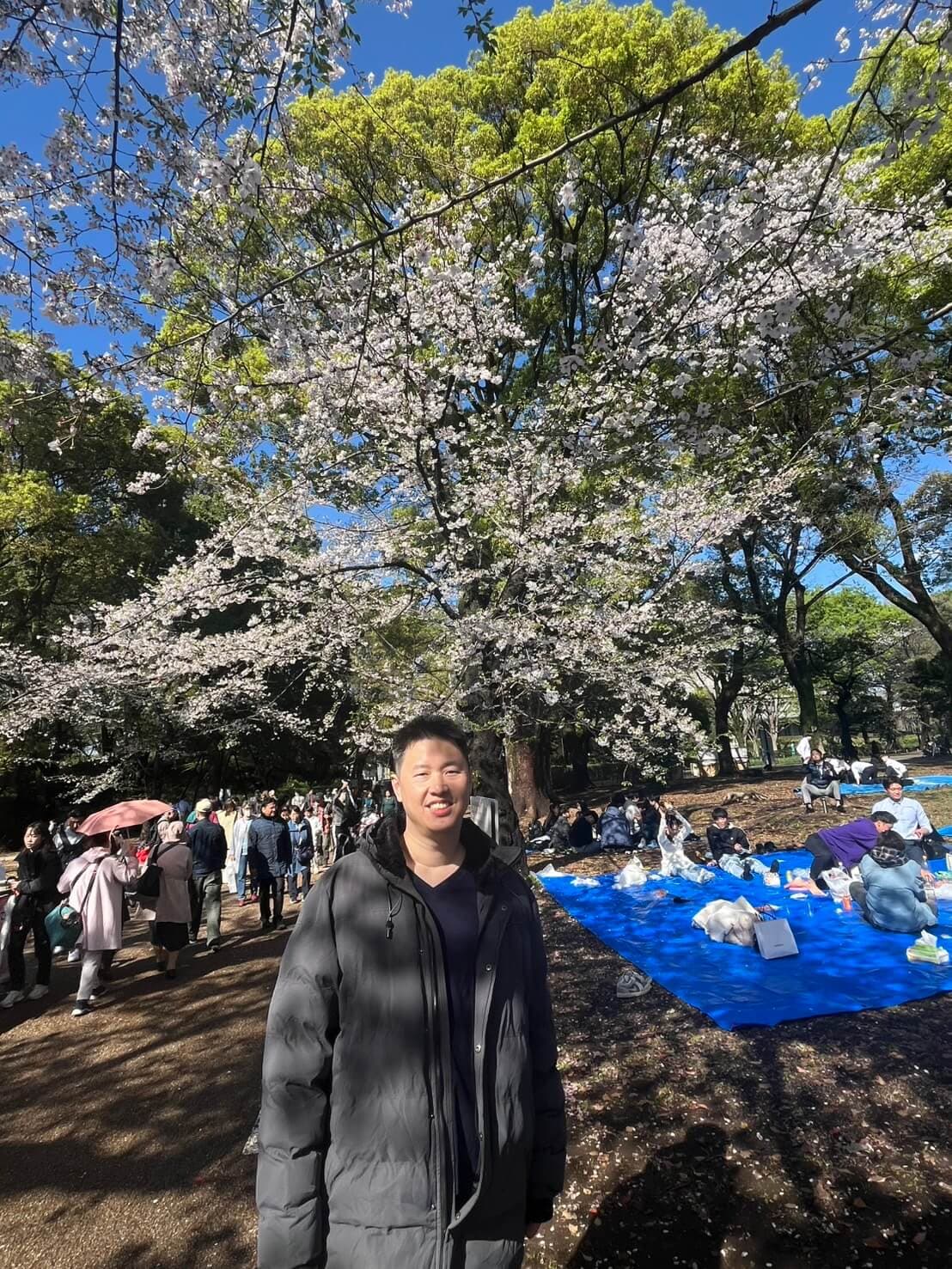 Varis Darasirikul standing beneath cherry blossoms in Tokyo, Japan
